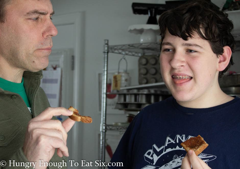 Man and teen boy sticking tongue out while eating toast.