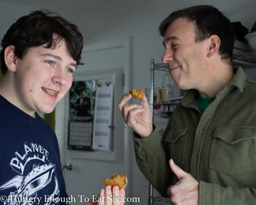 Teen male and man eating bites of Vegemite muffins. 