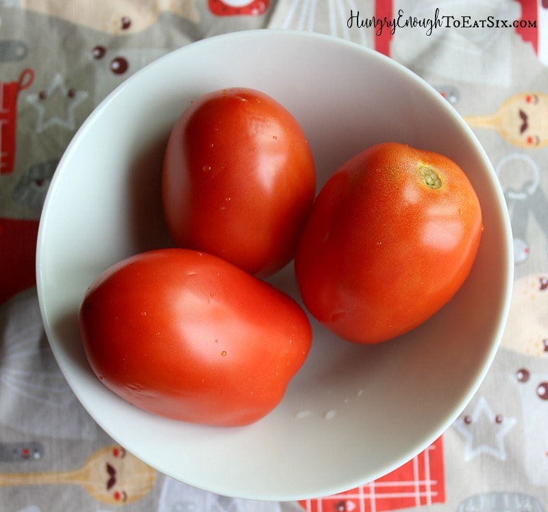 Three red ripe plum tomatoes in a white bowl.