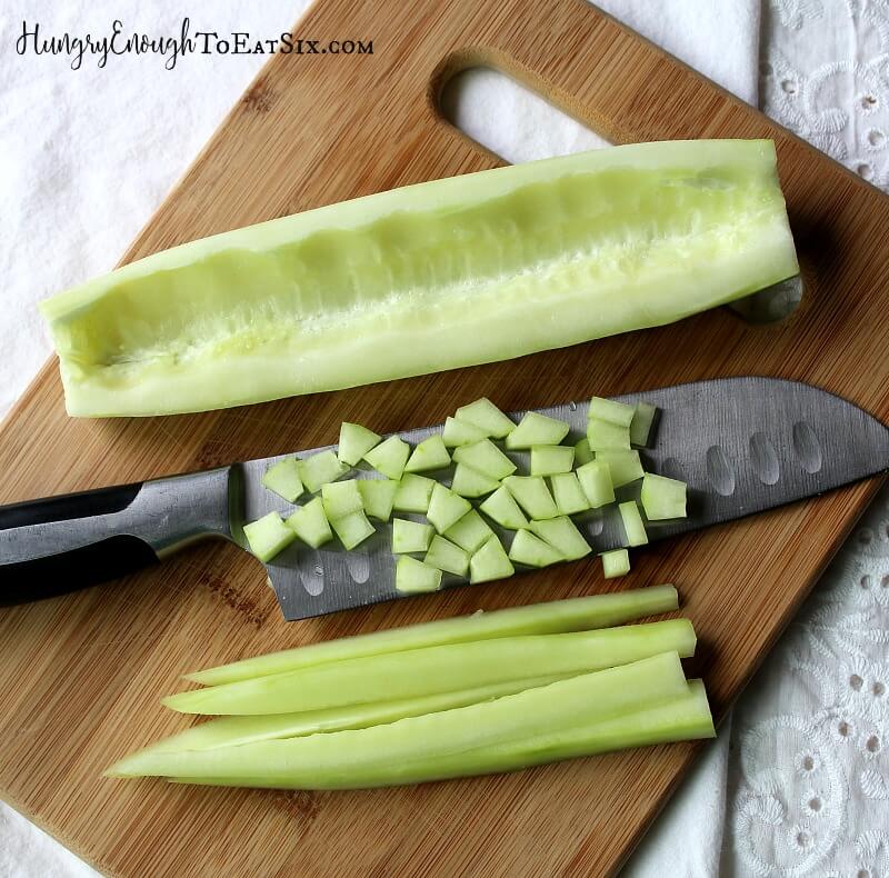 Cucumbers on a cutting board, sliced in half and diced with a knife under the diced bits.