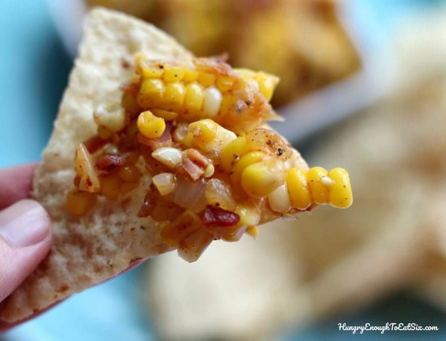 Image of hand holding tortilla chip with Corn, Vidalia Onion and Bacon Salsa on it.