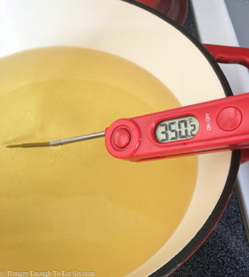 Digital thermometer with needle in oil in a white pan.