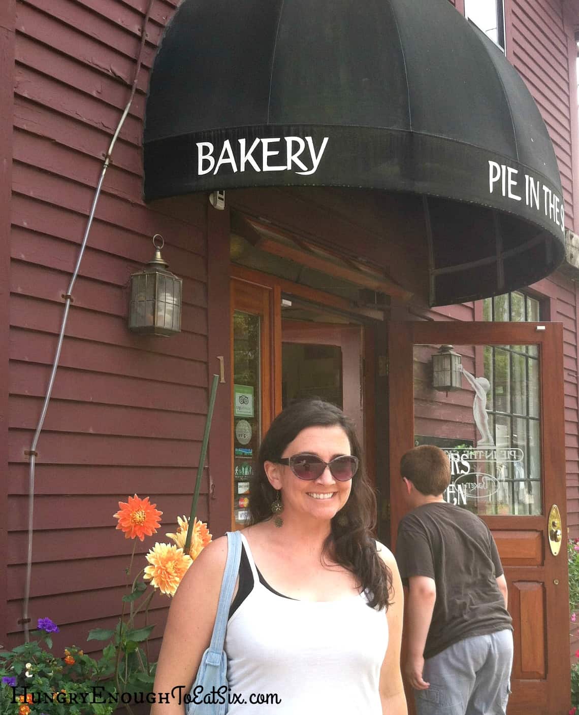 Woman in sunglasses posing outside bakery entrance.