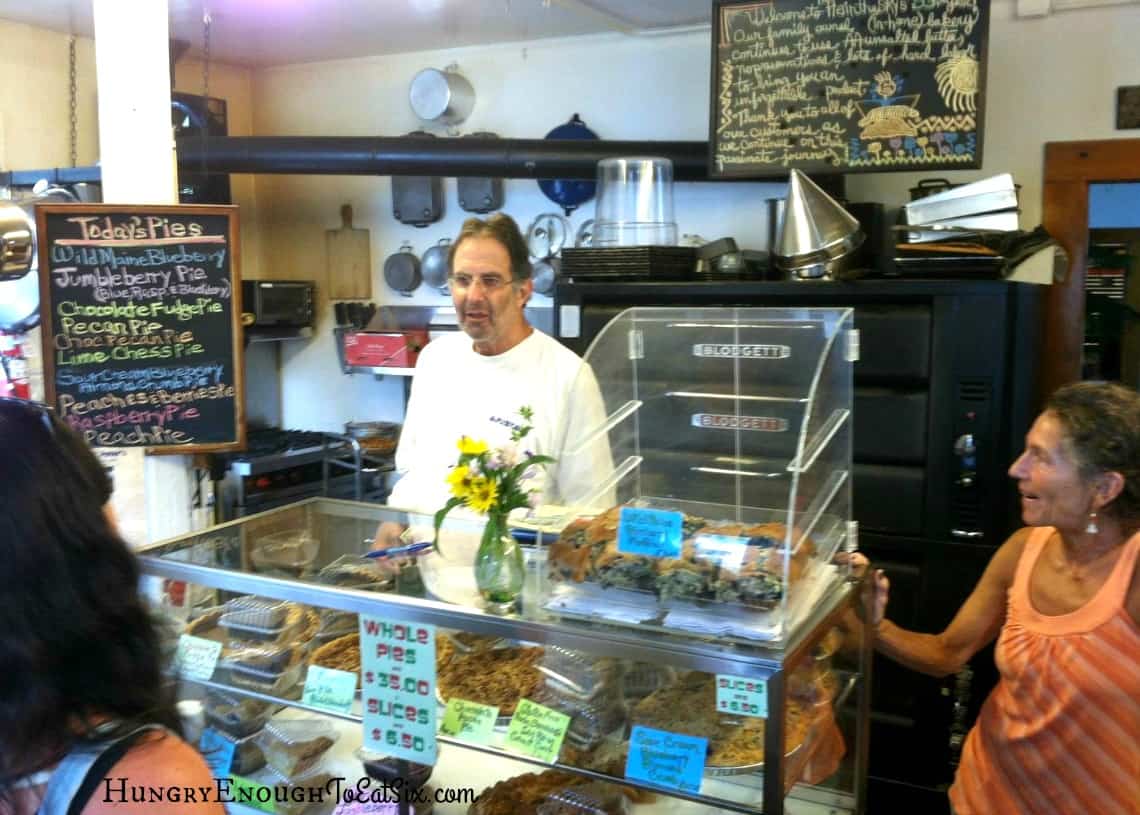 Man behind a glass bakery case with baked goods inside.