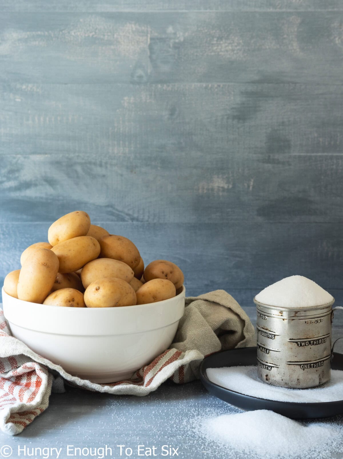 Bowl of potatoes next to a measuring cup of salt.