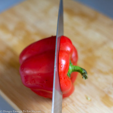 Knife slicing through the top of a red pepper.