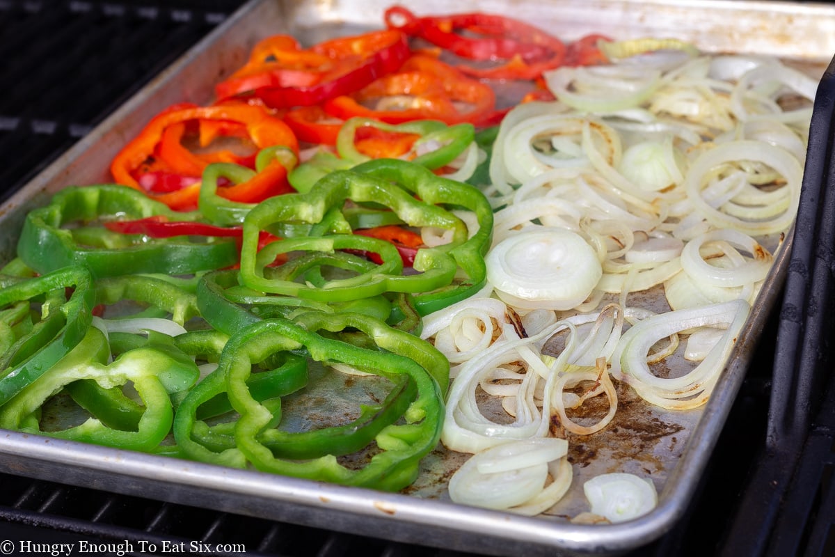 Sliced red and green peppers and sliced onions on a baking sheets