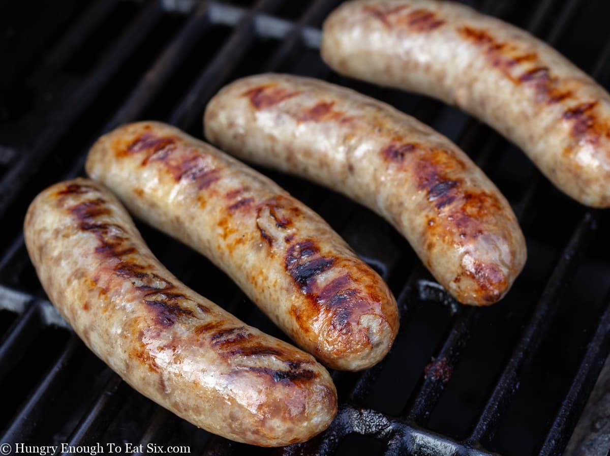 Four sausages grilling on a gas grill.