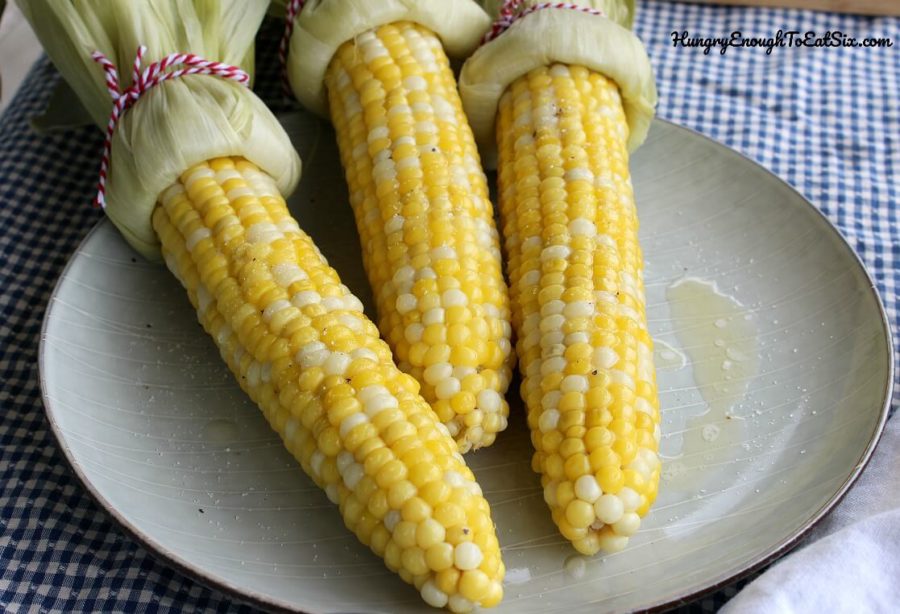 Cooked ears of corn with husks tied back, melted butter and spices on corn. 