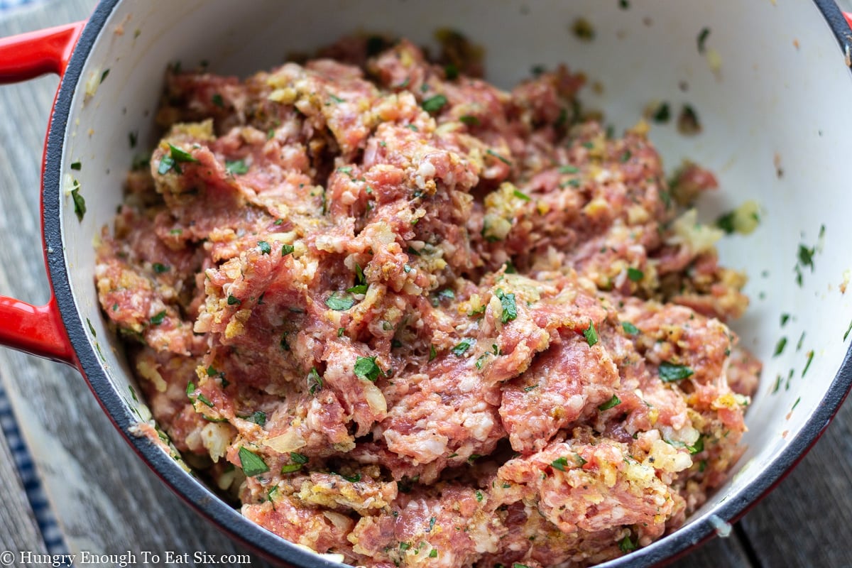 Meatball meat mixture with green flecks in a Red and white bowl.