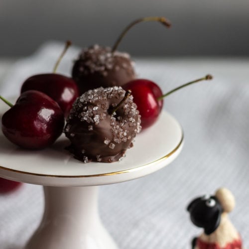 Small white pedestal holding plain and chocolaty cherries.