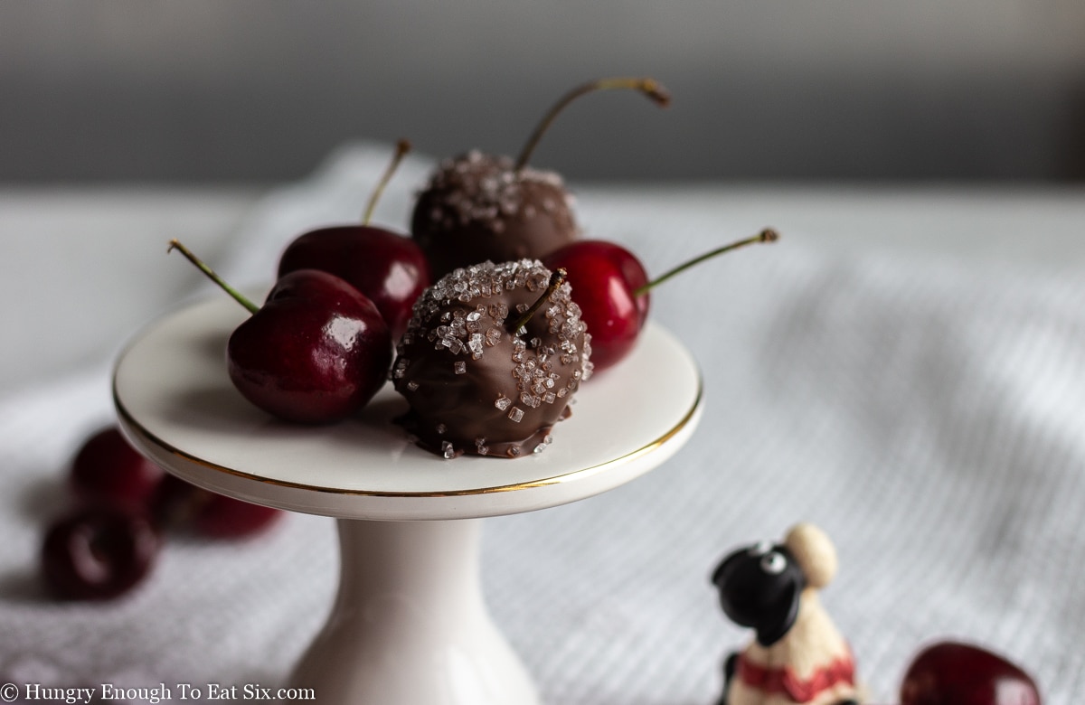 Plain and chocolate covered cherries on a white cake stand with a little sheep below.