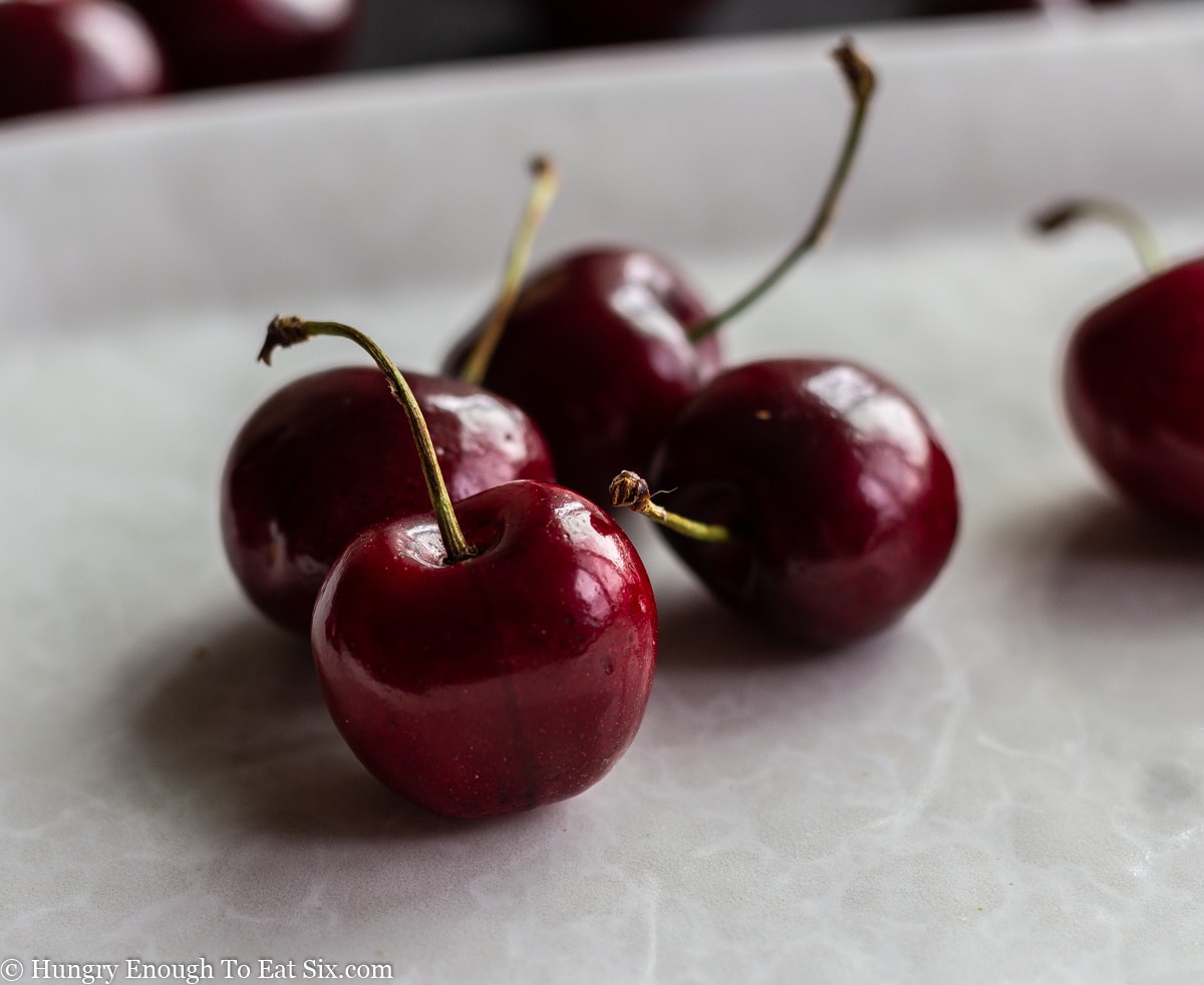 Red sweet cherries with stems sitting on a white platter.