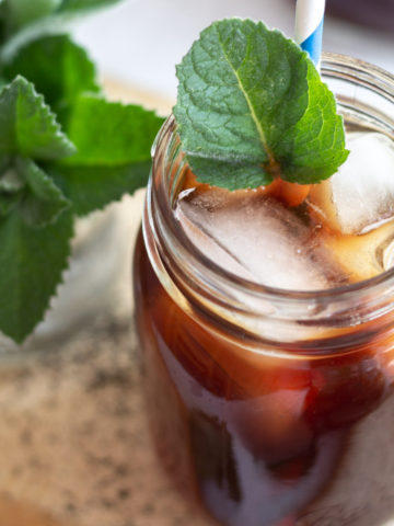Glass jar with dark iced tea, ice cubes and fresh bright green mint leaves.