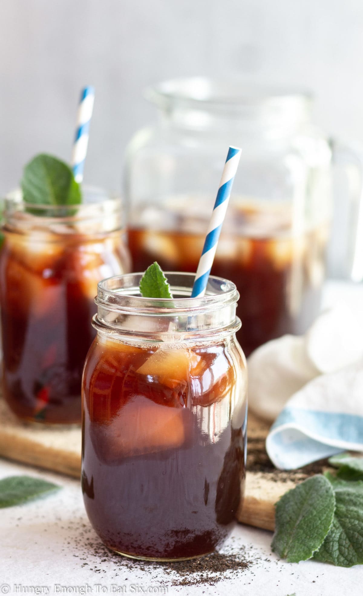 Medium sized mason jar holding iced tea and ice cubes with more containers of tea in background.