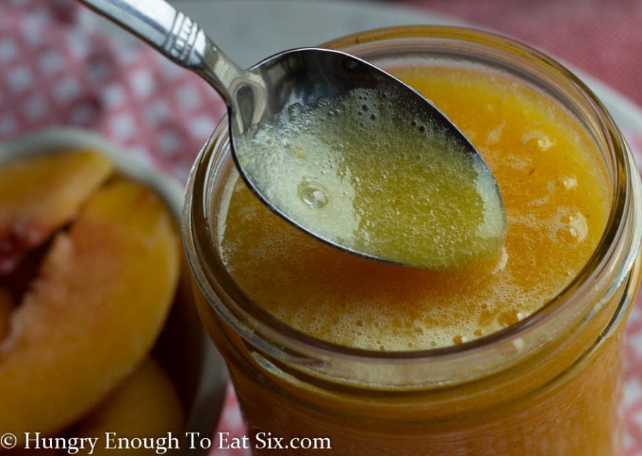 Small mason jar with peach nectar, spoon dipped in.