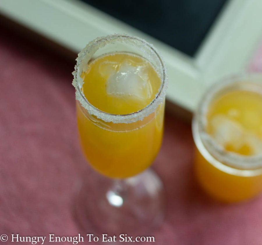 Champagne flutes with sugared rims filled with peach margarita and ice.
