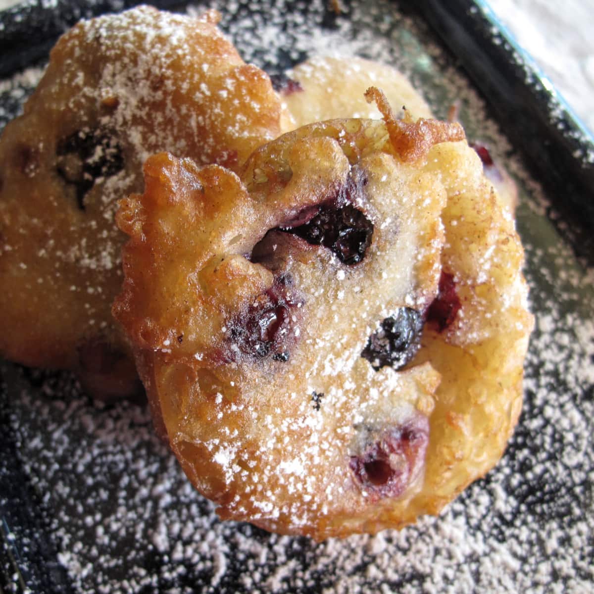 Blueberry fritters on a black plate.