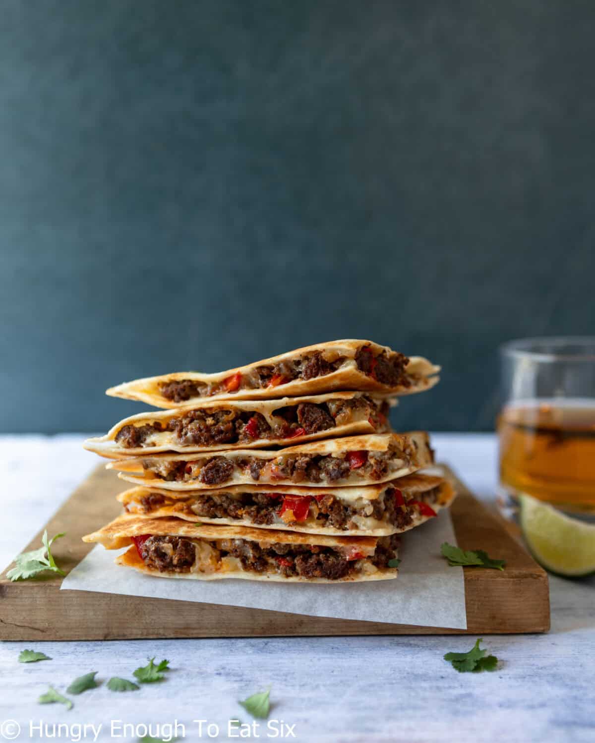 Sliced quesadilla wedges stacked on a cutting board.