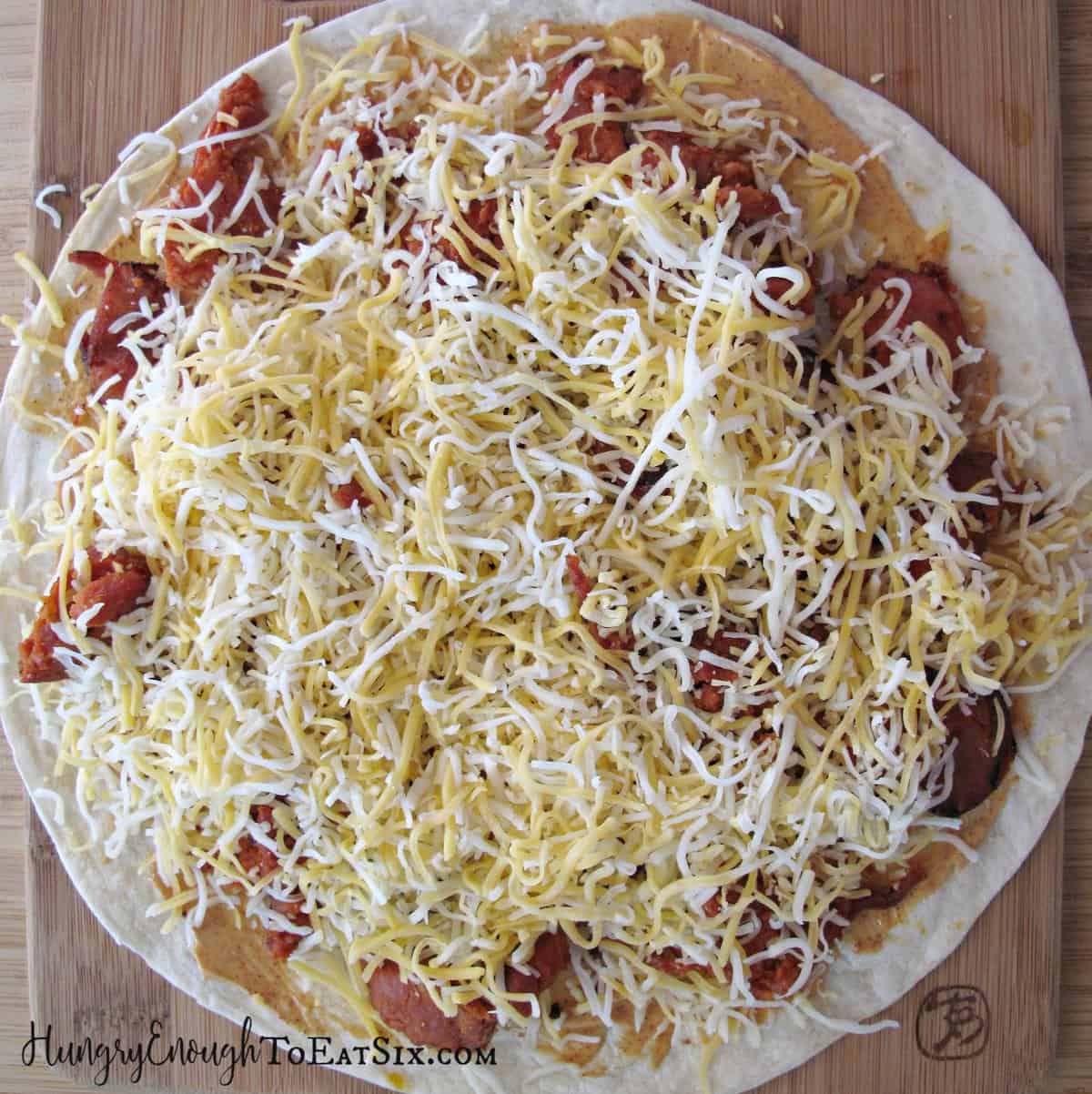 Tortilla topped with meat and shredded cheese.