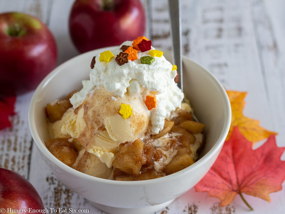 White dish of vanilla ice cream topped with apples, whipped cream, and sprinkles
