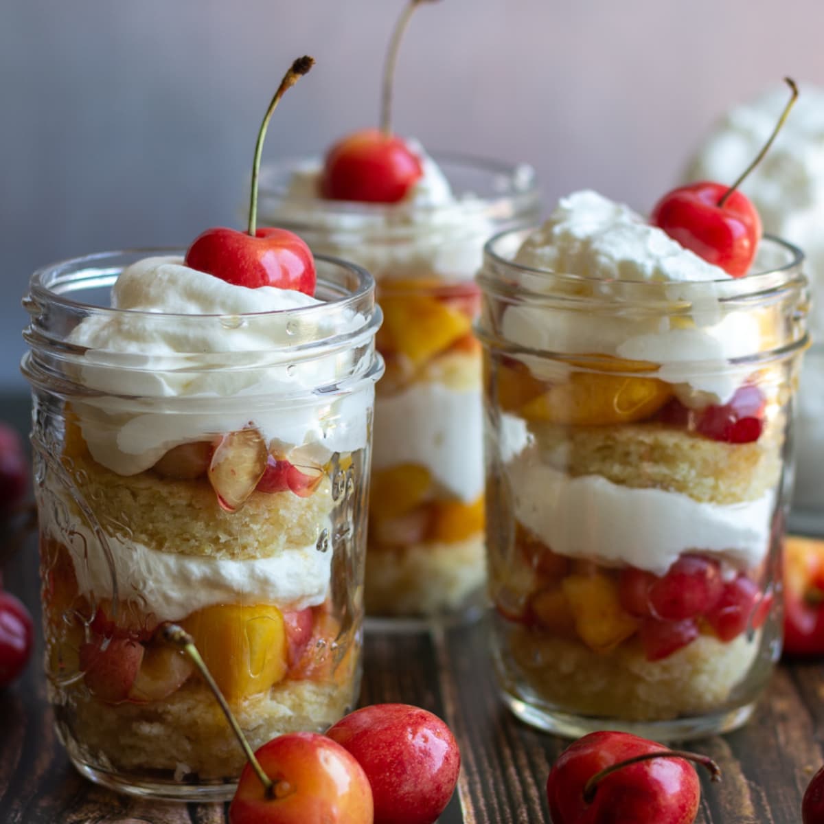 Three glass jars with cherry nectarine layered trifles.