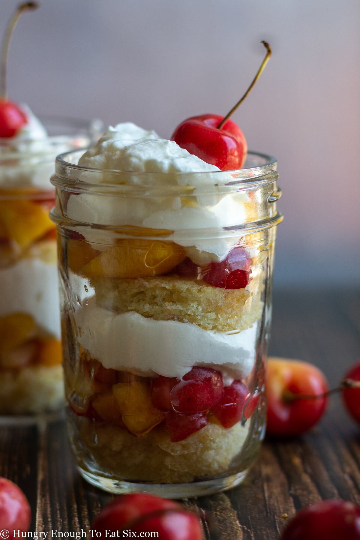 A cherry nectarine trifle in a glass jar with a cherry on top.