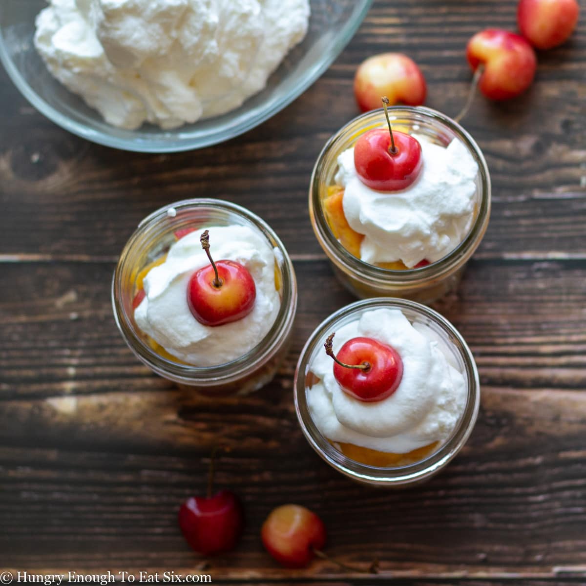 Cream topped trifles in mason jars with cherries on top.