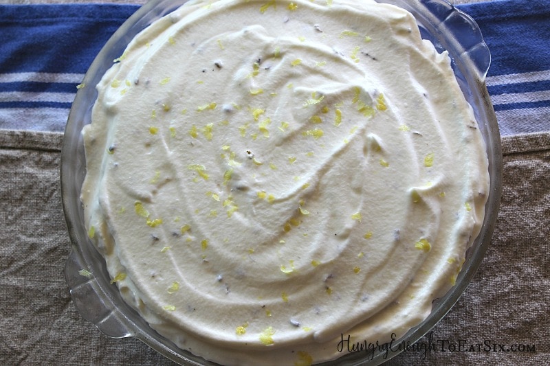 Glass pie dish with a chilled pie that has a whipped cream top, with lemon zest and lavender.
