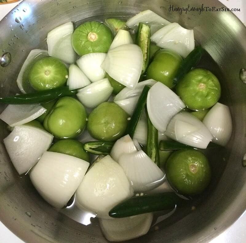 Tomatillos and chunks of onion simmering in a pot.
