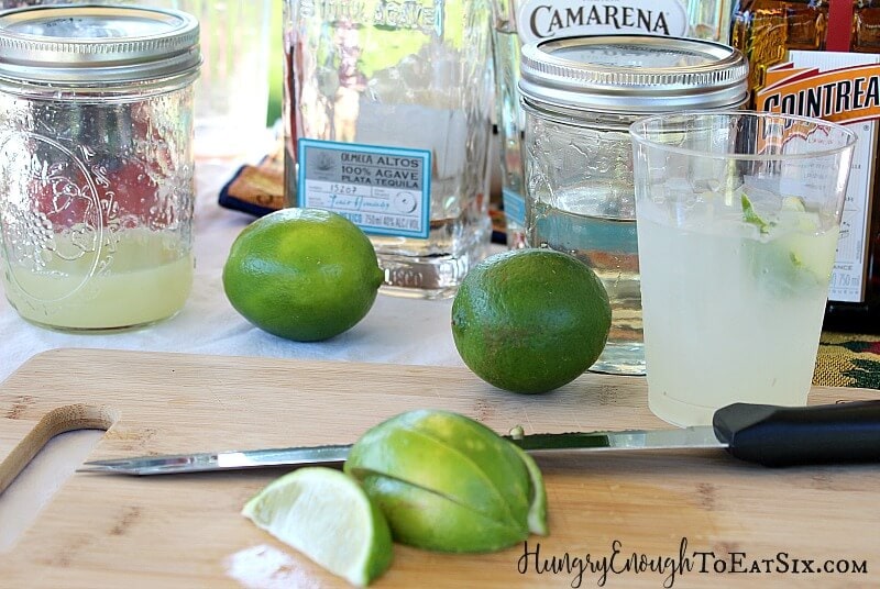 Limes on a wood cutting board next to jars of margarita mix