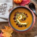 Swirls of sour cream and toppings on spicy pumpkin soup in a bowl.