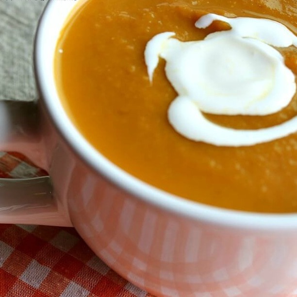 Pumpkin soup with a dollop of sour cream in a white cup.