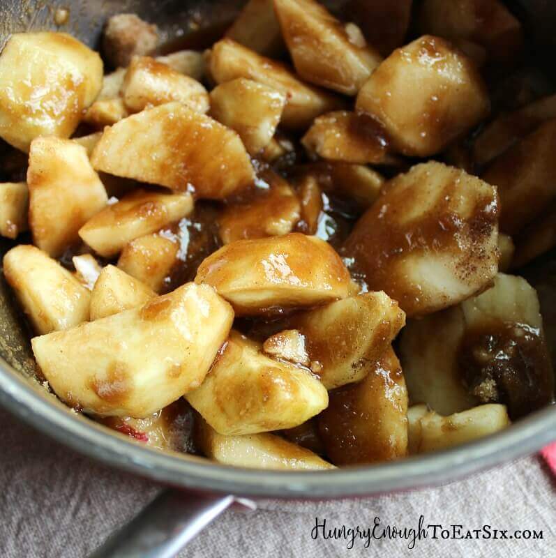 Sliced apples in a bowl, tossed in brown sugar and spices.