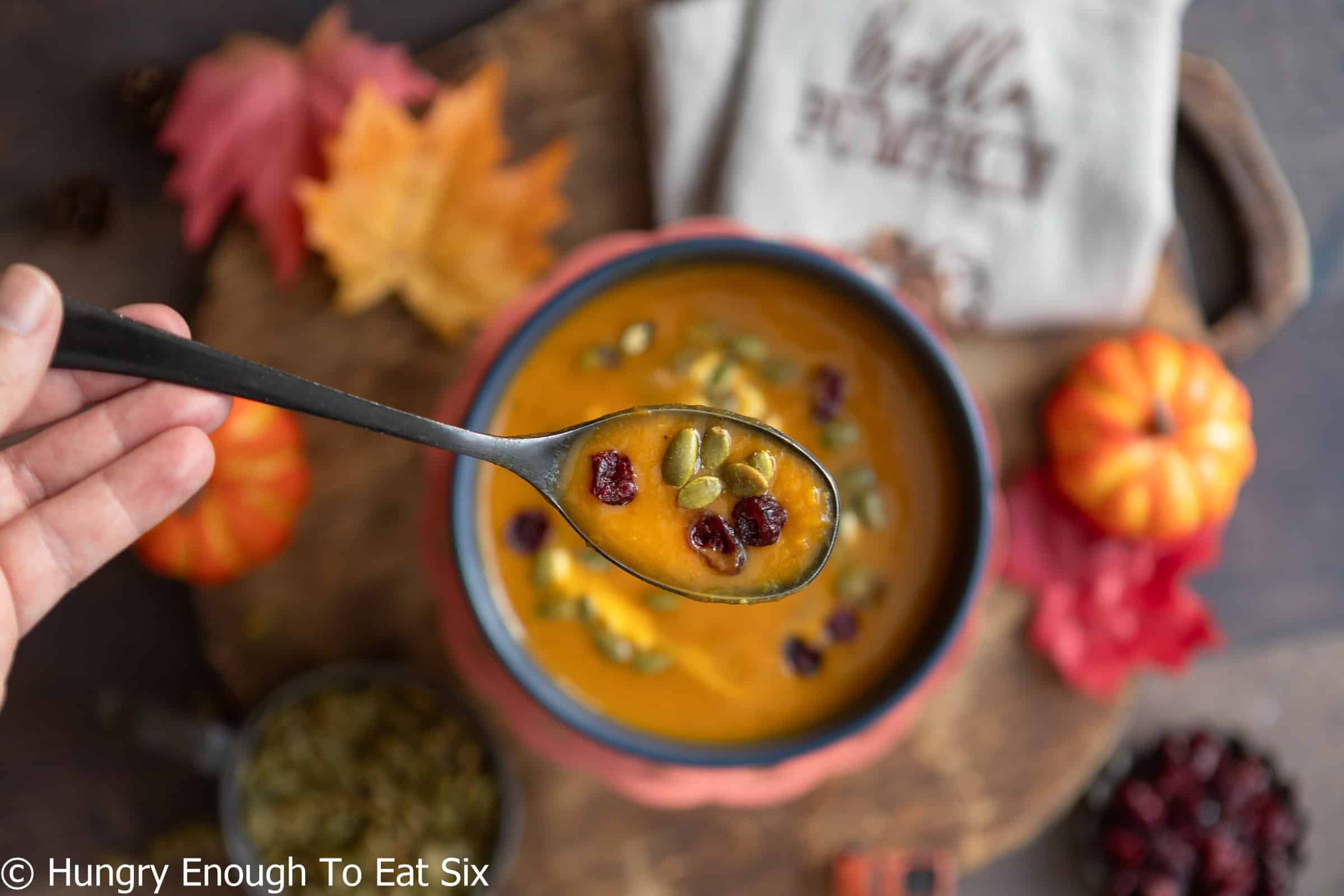 Spoonful of spicy pumpkin soup over the bowl.