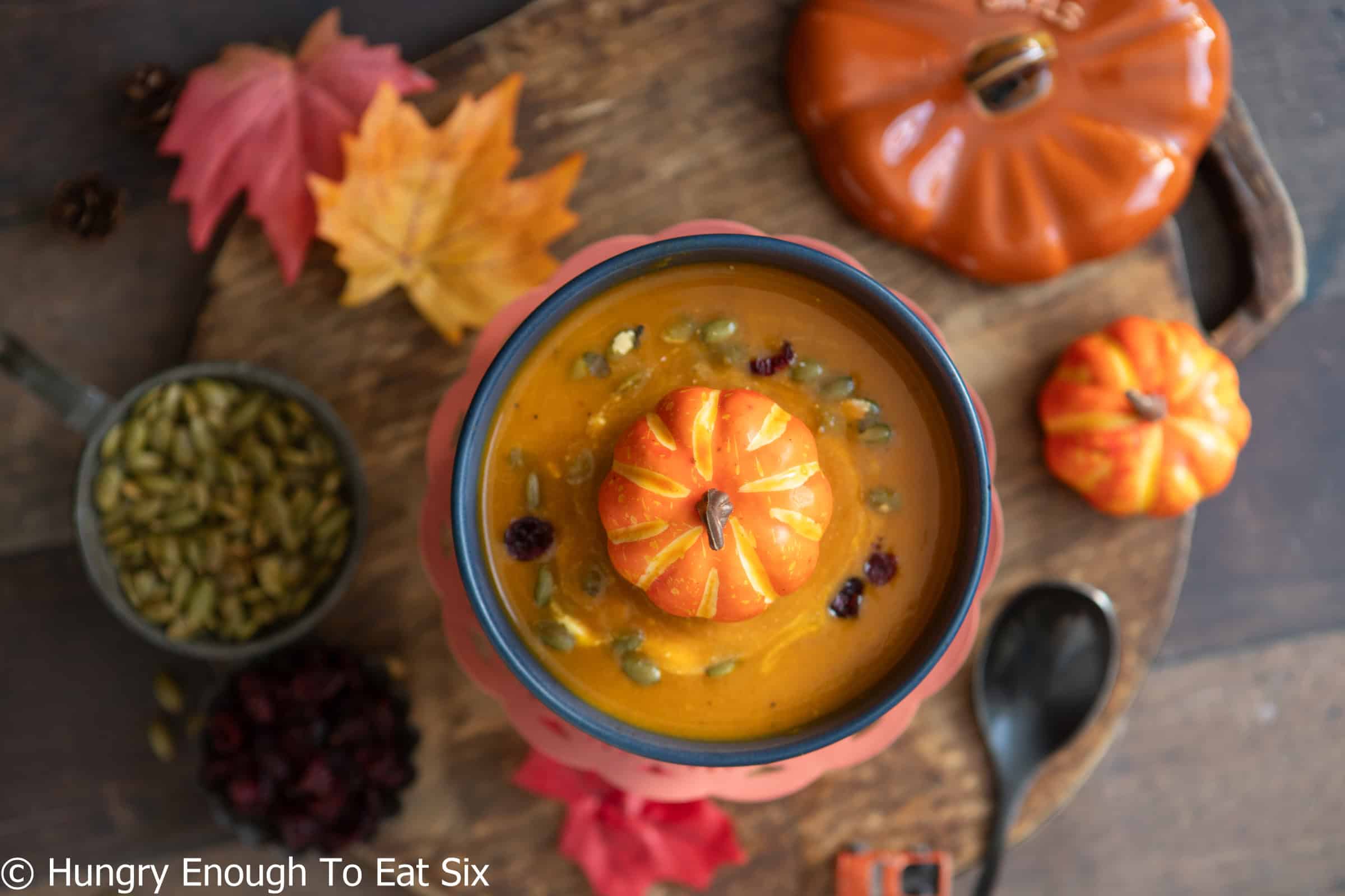 Bowl of spicy pumpkin soup with decorative pumpkin on top.
