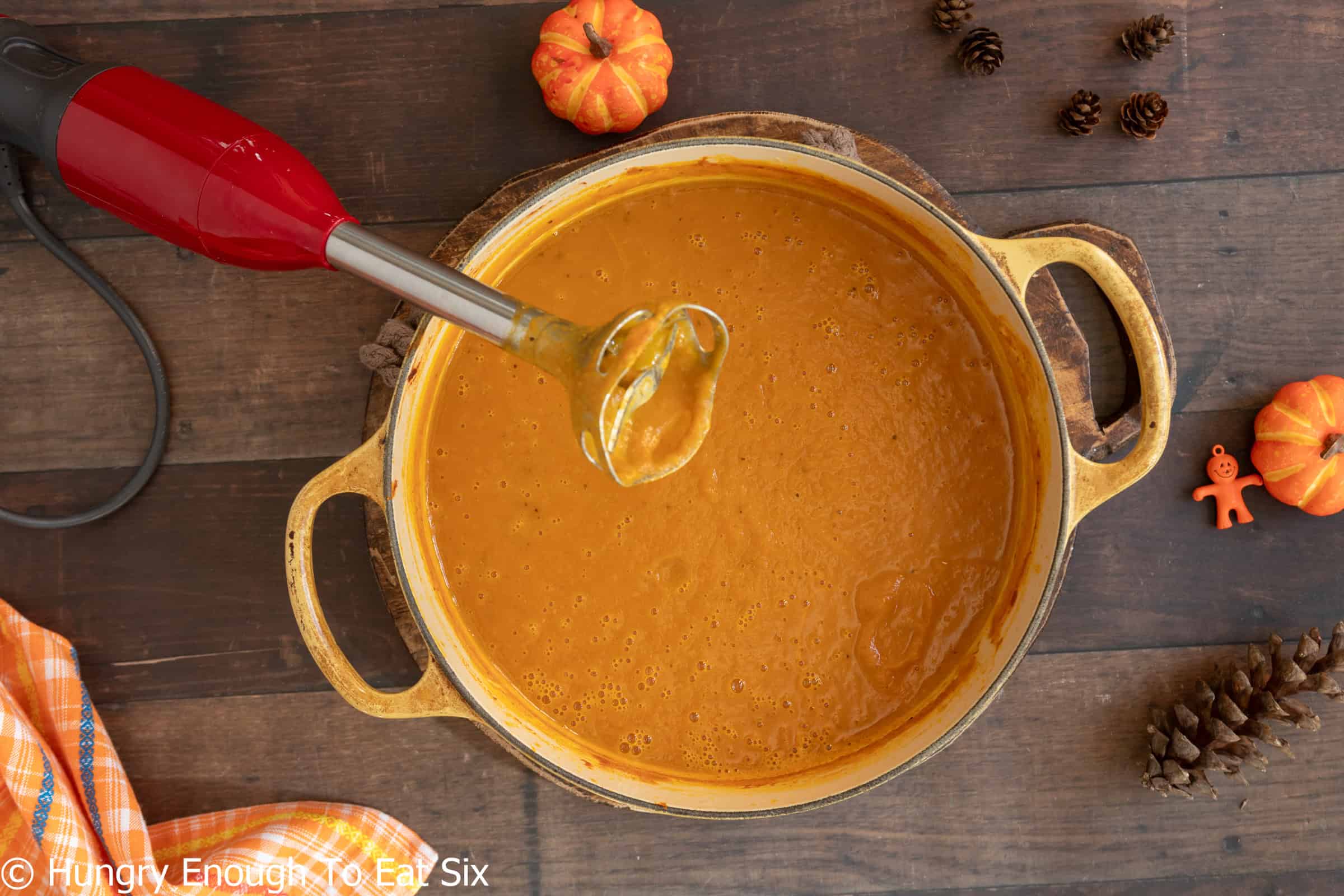 Pureed spicy pumpkin soup in a pot with an immersion blender.
