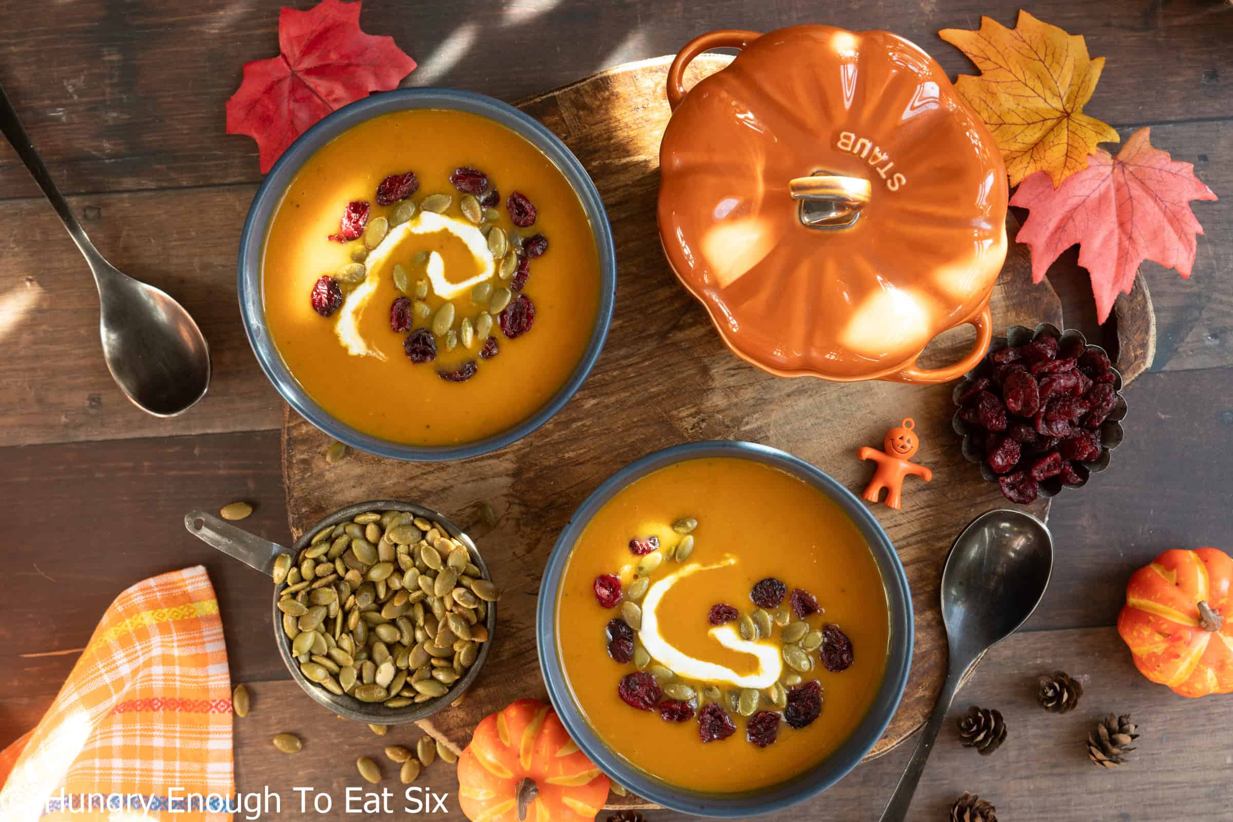 Two bowls of spicy pumpkin soup topped with sour cream and pepitas.