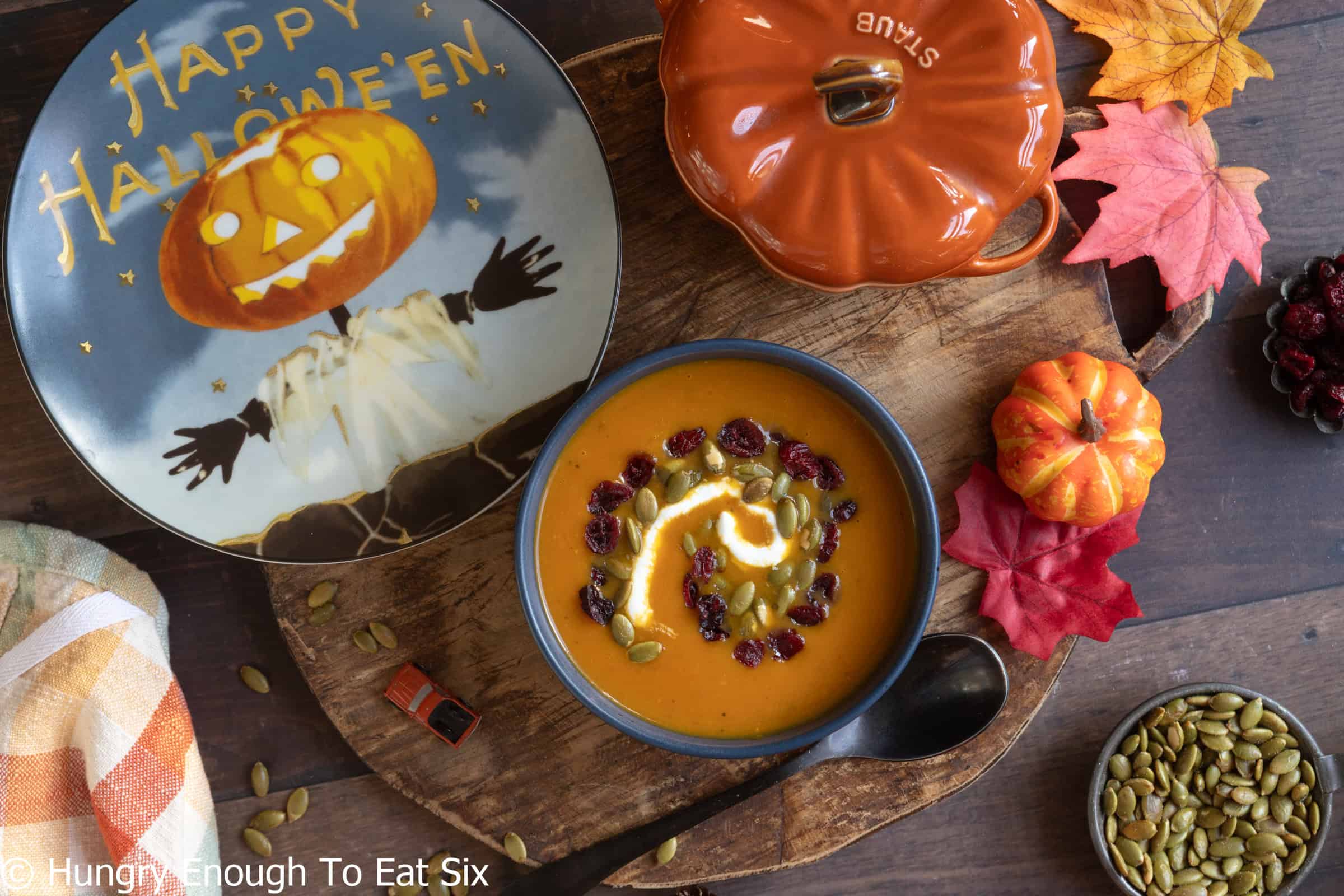 Bowl of spicy pumpkin soup next to a Halloween decorative plate.