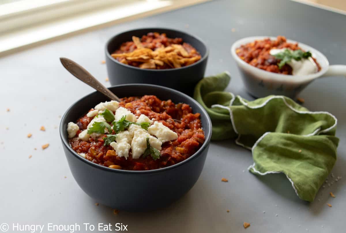 Three bowls of chili with cheese on top.