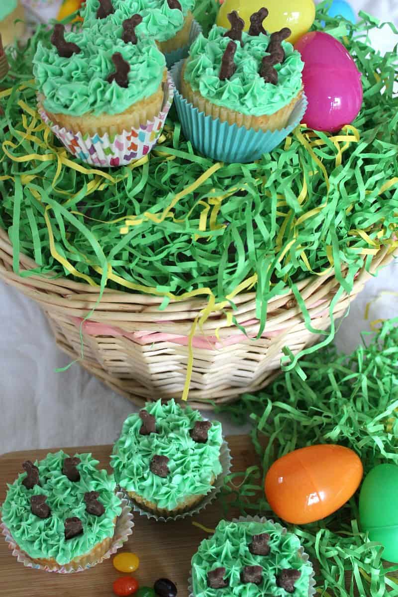 Easter basket with green paper grass, plastic eggs, and Easter Surprise Cupcakes with green frosting.