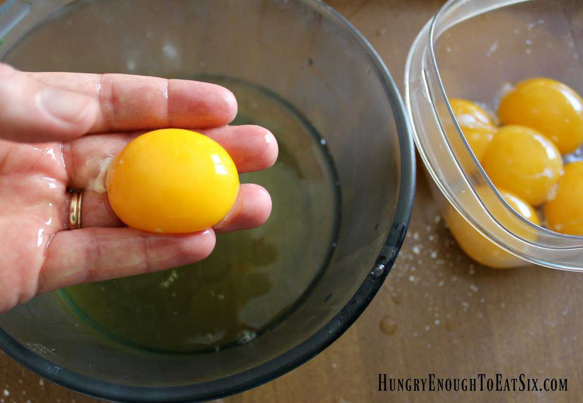 Egg yolk in a hand over bowl of egg whites.