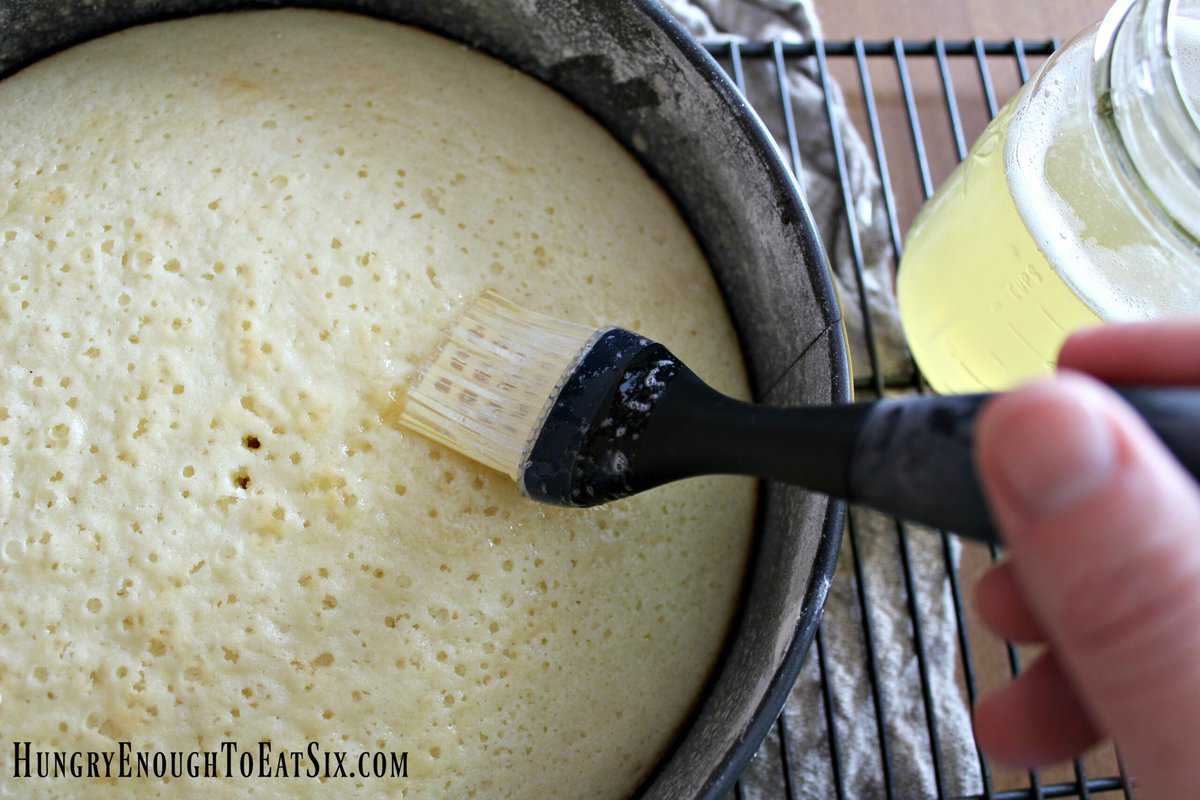 Pastry brush over white cake round in pan.