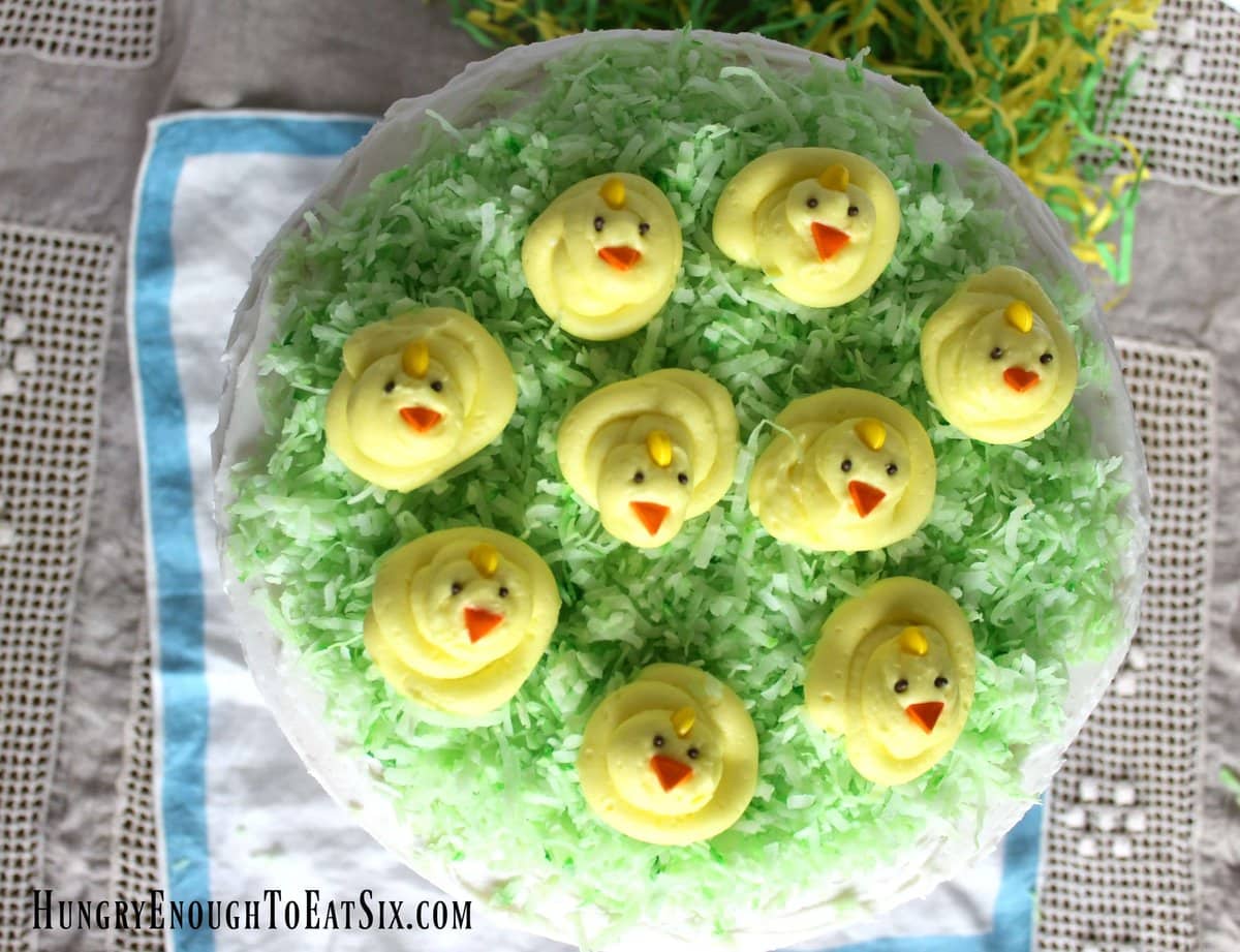 Think Spring and eat it too! This cake is full of bright lemon flavor, buttercream, and happy spring chicks on coconut grass,