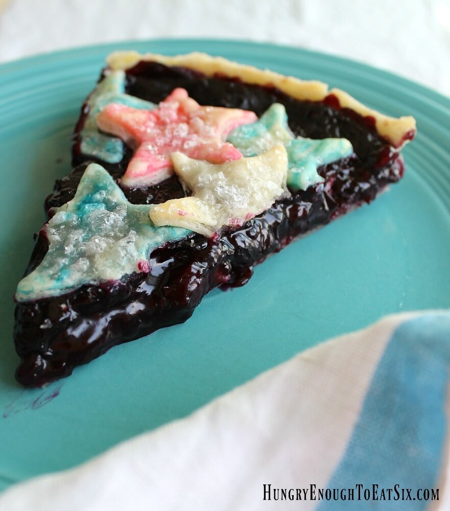 A slice of cherry-blueberry tart with red, white and blue stars on top, resting on a blue plate.
