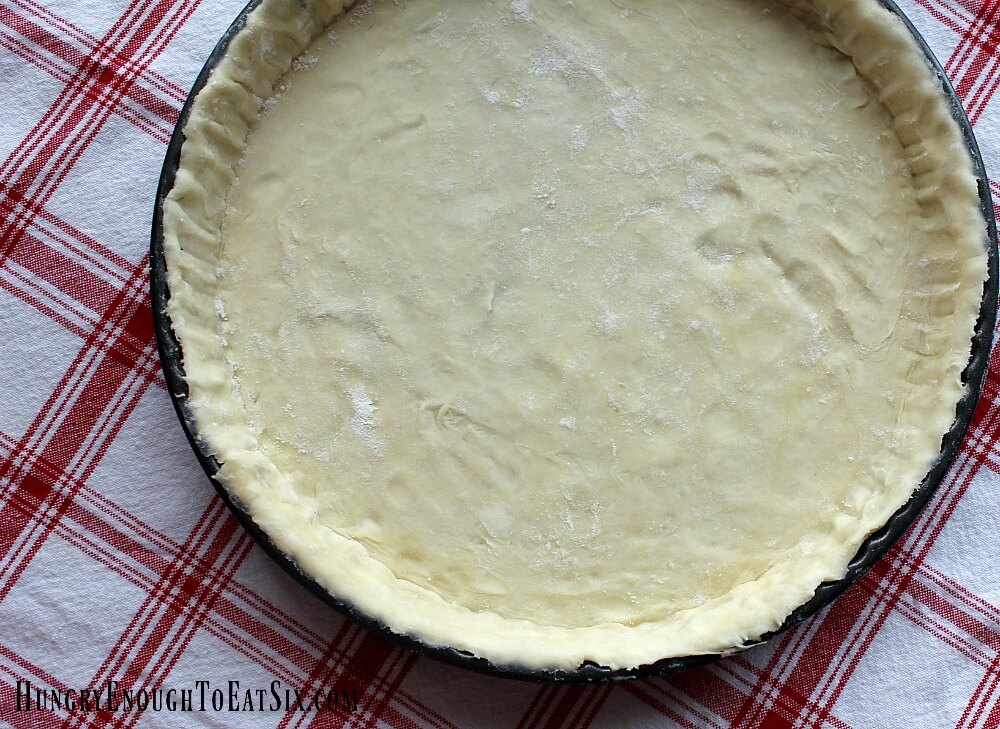 Pastry dough pressed into a round tart pan, red and white plaid cloth in background.