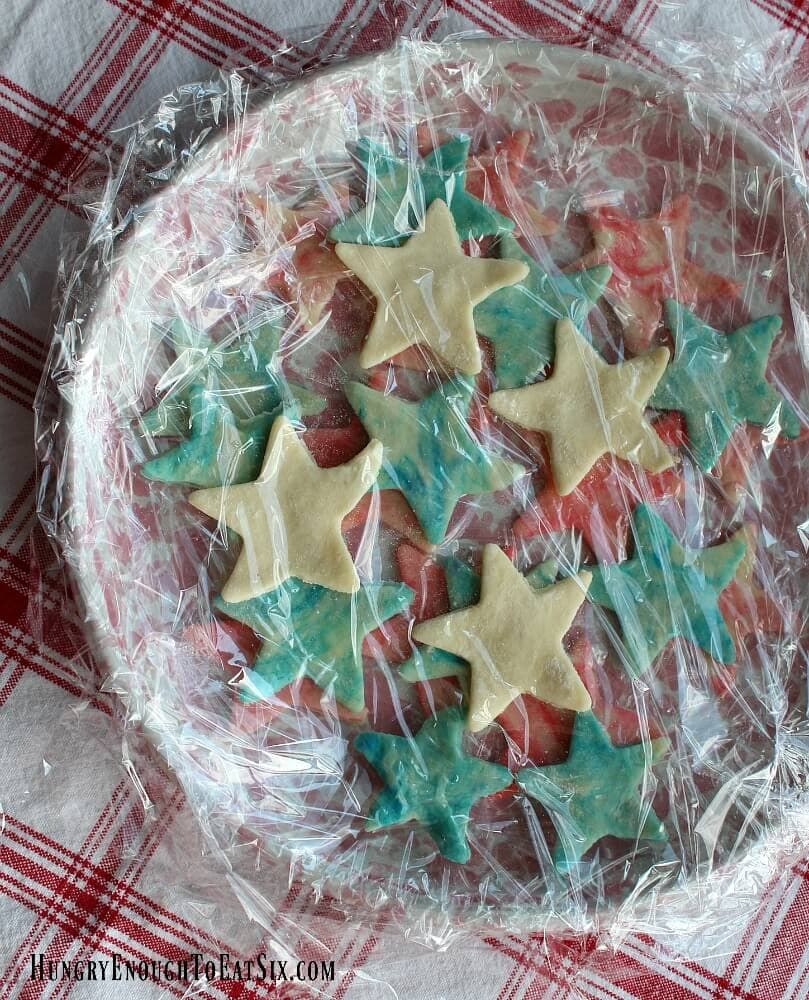 Red, white and blue pastry stars on a pink plate under a few sheets of plastic wrap.