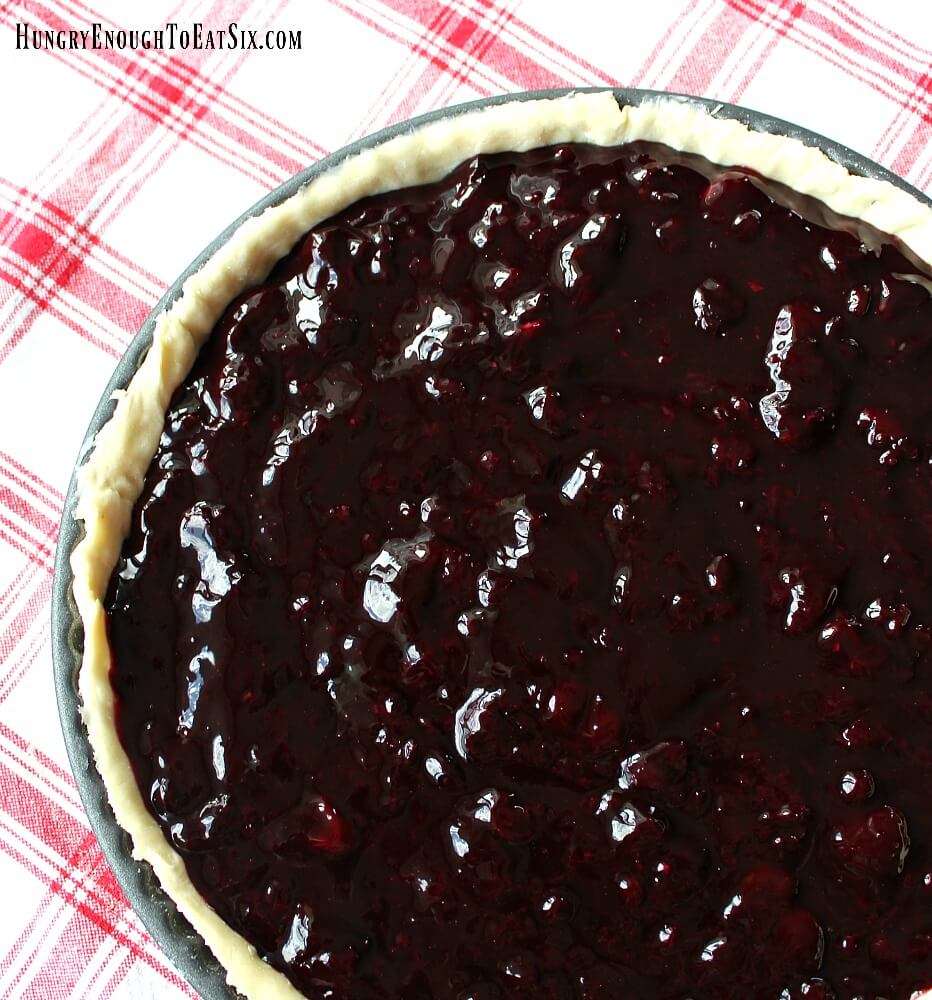 Tart shell filled with the dark cherry blueberry filling, red and white plaid cloth  in background.