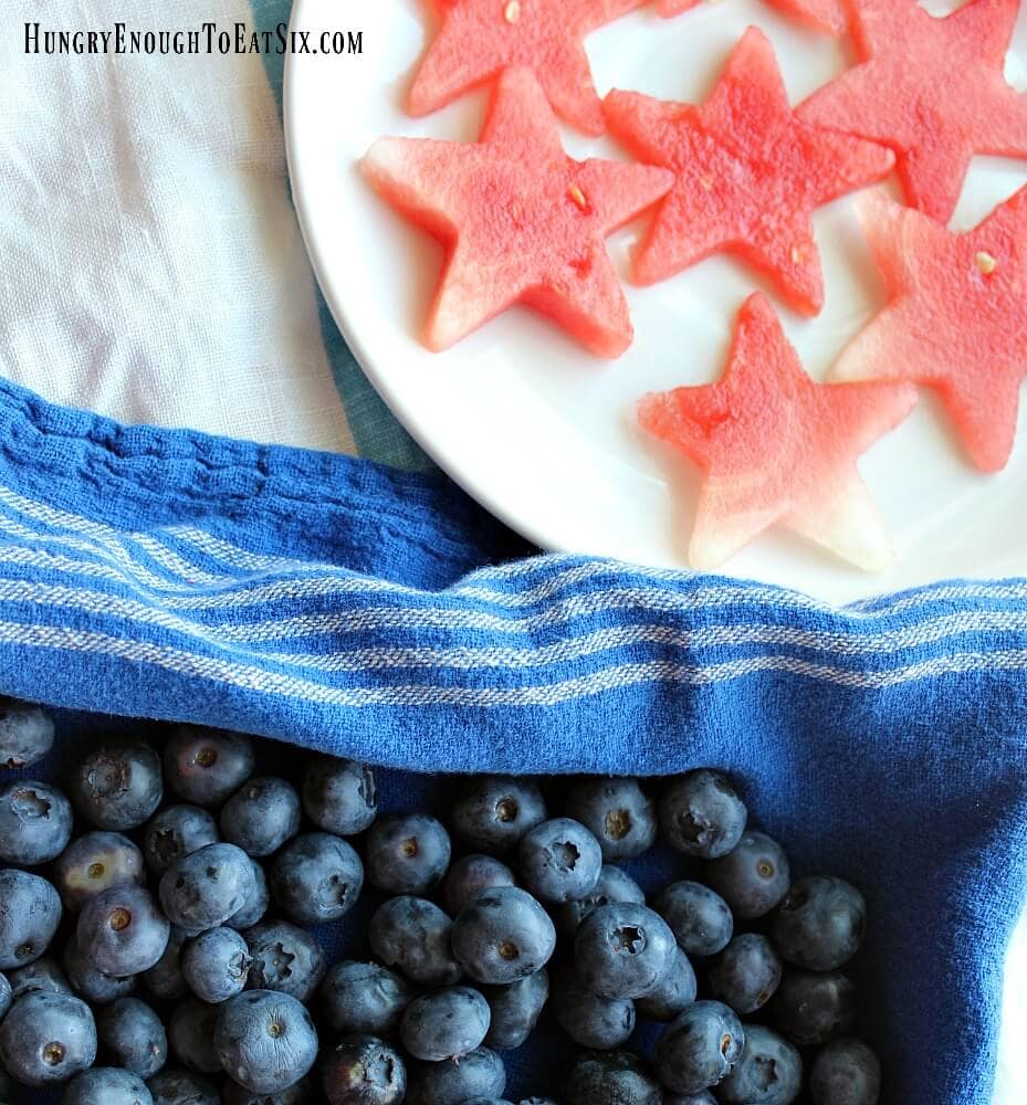 Watermelon stars on a white plate next to a blue towel and blueberries.