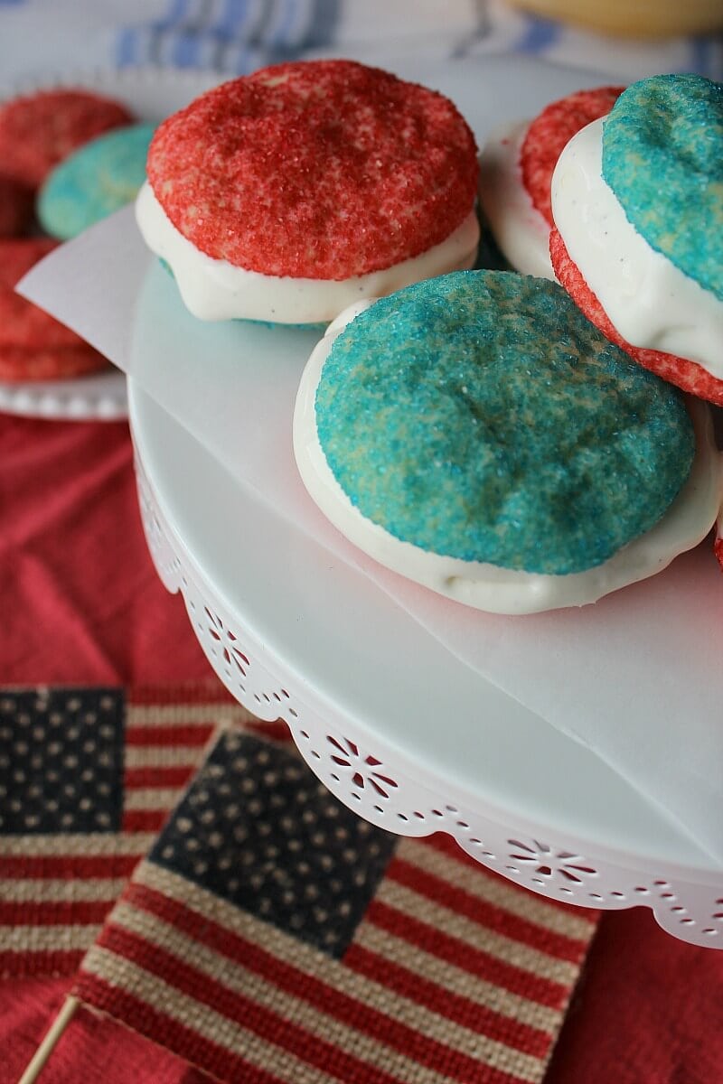 Ice cream sandwiches with red and blue sugar cookies and white ice cream, on a white pedestal.